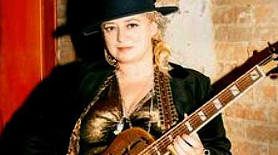 lady guitarist with black hat holding guitar, red curtain background
